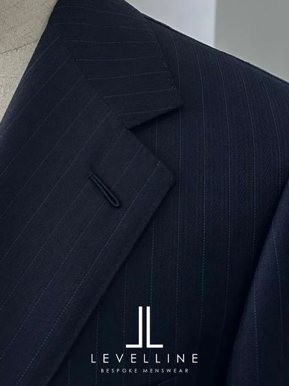Our brand logo on this bespoke navy blazer signifies a commitment to quality. The peak lapel and fine fabric texture are hallmarks of our custom formalwear.