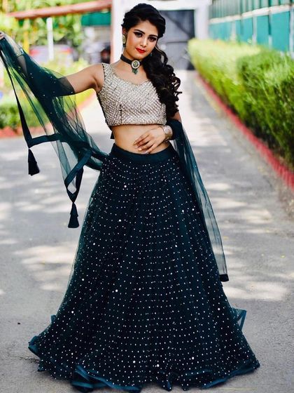 A full-length shot of a client in a dark green sequined lehenga with a contrasting gold blouse. This is a chic and modern combination for a festive occasion.