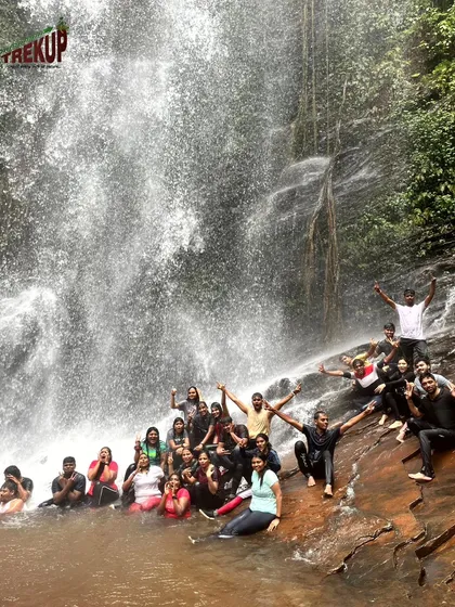 A group posing for a photo under the refreshing spray of a waterfall on the Kodachadri trail.