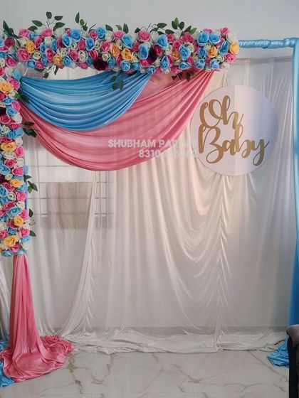 A beautiful "Oh Baby" backdrop with pink and blue drapes and an artificial flower border.