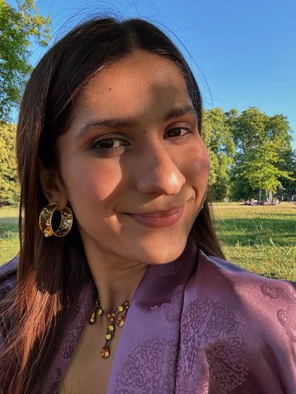 A sunny day selfie in a park. The purple brocade jacket and gold jewelry create a rich, warm look.