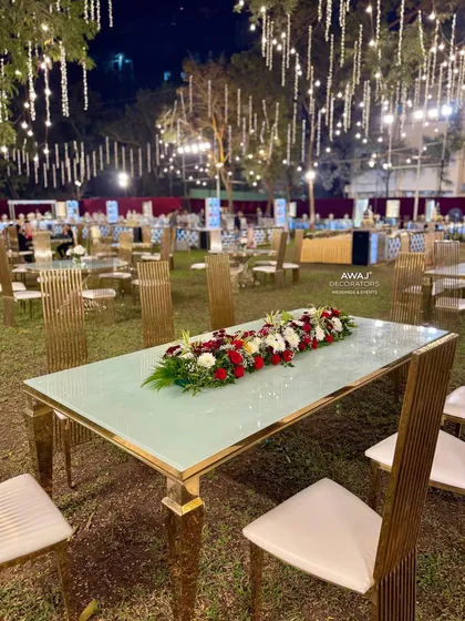 A modern, gold-trimmed dining table with a long floral runner, set against the backdrop of a beautifully lit event space.