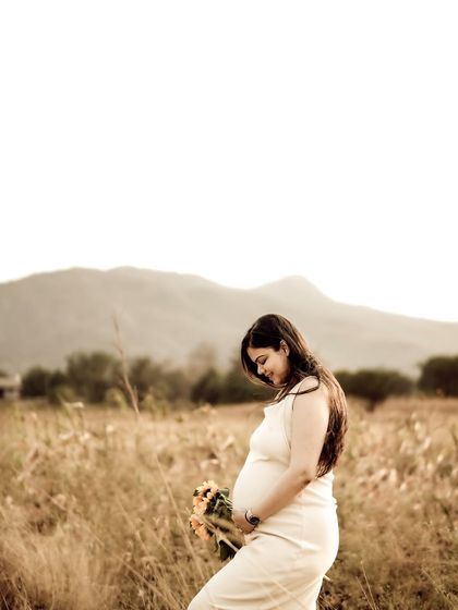 A beautiful solo portrait of the mom-to-be in a white dress, standing in a field and looking down at her bump. The image is full of peace and serenity.