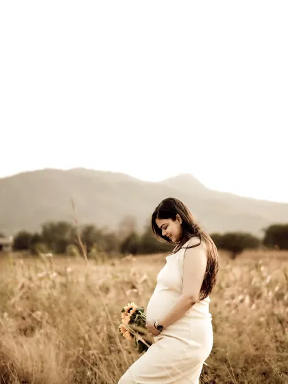 A beautiful, minimalist portrait of the mom-to-be in a white dress, standing in a field at golden hour. The simplicity of the shot highlights her natural grace and the beauty of the moment.