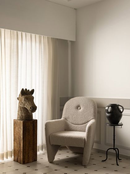 The master bedroom at Ecru Maison is a serene space defined by soft neutrals and organic forms. We designed this plush, tufted armchair to create a cozy reading corner, complemented by sculptural art and decor.
