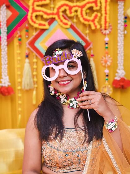 A fun-loving bride posing with a "Bride" prop at her haldi ceremony.