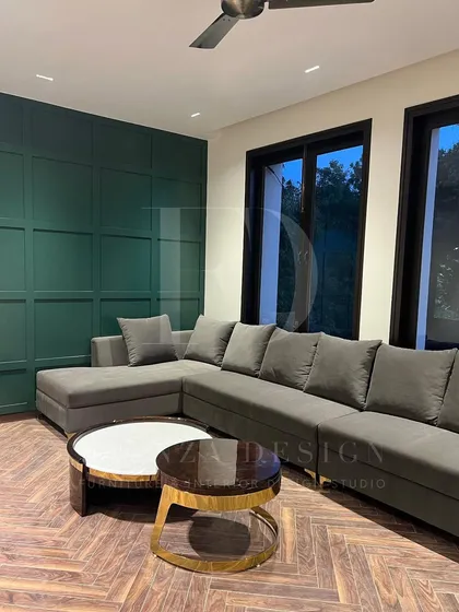 A grey L-shaped sectional set against a dark green paneled wall. The herringbone wood floor and nested marble coffee tables with brass accents complete this moody and sophisticated living room.