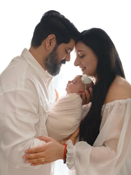 A tender moment between new parents and their baby. The backlighting creates a beautiful, soft halo effect, adding to the dreamlike quality of the image.