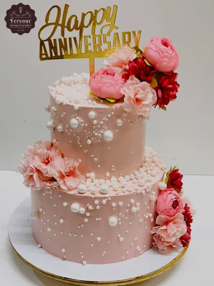 A lovely two-tier anniversary cake in a soft pink hue, decorated with edible pearls and a mix of fresh pink and red flowers. This design is a perfect example of how I use whipped cream to create a beautiful, textured finish.
