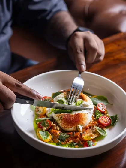 A refreshing bite of the Burrata Salad, with its creamy center spilling out over fresh tomatoes and pesto.