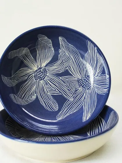 This is my 'Dutch Iris' pasta bowl set, inspired by the delicate flower. The design is hand-carved into the clay, creating a beautiful contrast with the deep indigo glaze. These bowls are perfect for sharing a cozy meal with loved ones.