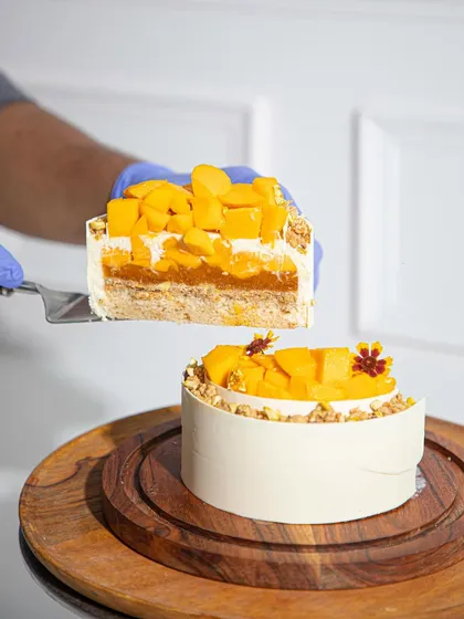 A hand holding a slice of our layered mango cake, showing the perfect structure and fresh ingredients.