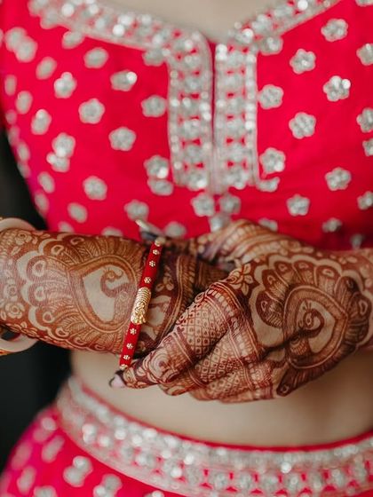 A close-up of the bride's hands, showcasing the intricate henna design and her beautiful red and white bangles.
