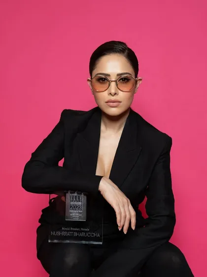 A portrait of Nushrratt Bharuccha with her award at the ELLE Graduates 2023 event. The clean pink background makes the subject and the trophy pop.