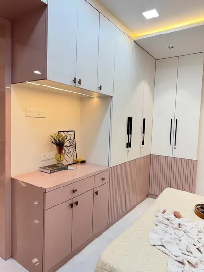A look at the functional side of our bedroom designs. This image highlights a seamless, wall-to-wall wardrobe in a soft pink and white dual-tone finish, with fluted panel details and an integrated dresser unit for maximum storage and style.