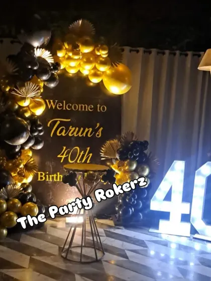 A chic black and gold themed decoration for a 40th birthday party. The setup includes a custom backdrop, an elegant balloon arch, and a large marquee number '40'.