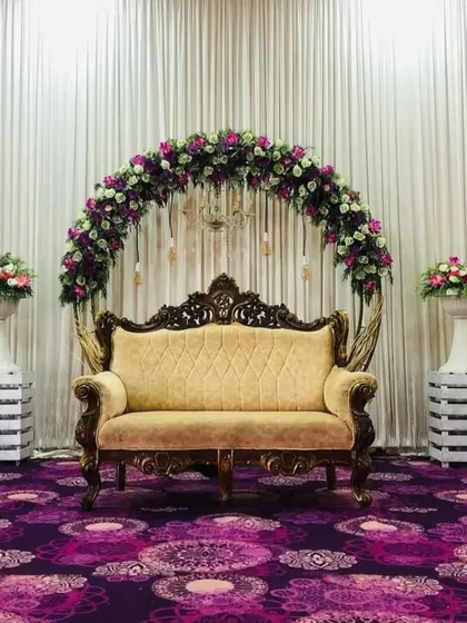 I designed this elegant stage for a ring ceremony, featuring a classic floral arch in purple and white. The ornate golden sofa provides regal seating for the couple, creating a perfect photo opportunity for their special day.