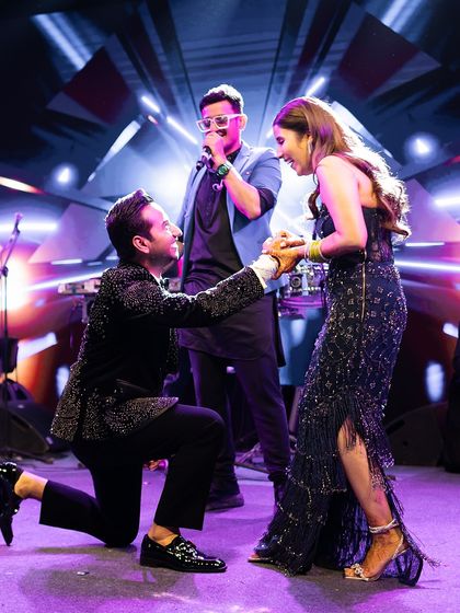 After the vows, the party begins. For this cocktail after-party, the groom serenades his bride on stage. Her midnight blue embellished gown by Shantanu & Nikhil was styled for glamour, movement, and a whole lot of fun.