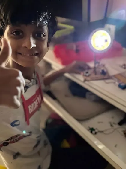 Summer time is build time. This young innovator gives a thumbs-up after successfully building and lighting up his DIY table lamp project. It's a great feeling to see your own creation work.