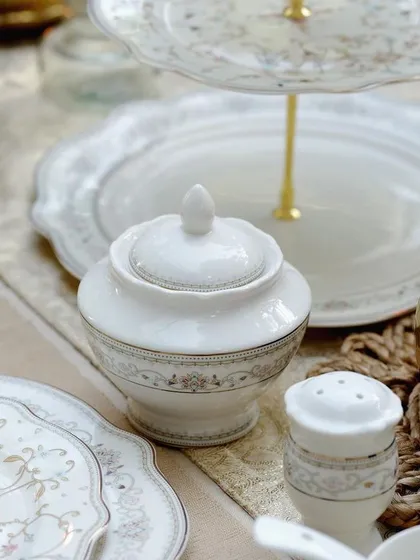 A styled shot of a Vigneto sugar bowl and other tableware on a beautifully set table. The warm, golden tones from the candle holder add a touch of luxury to the scene.