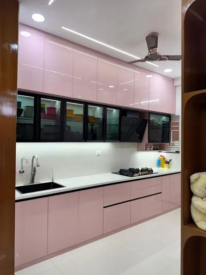 A sleek, modern kitchen featuring high gloss pink laminate cabinets and black profile handles. The smoked glass upper cabinets add a touch of elegance and allow for displaying crockery.