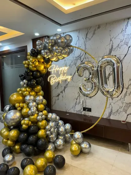 For a sophisticated and masculine theme, I use a combination of black, gold, and silver balloons on a slim golden ring. This style, shown celebrating a 30th, is perfect for a surprise anniversary party in a modern home.