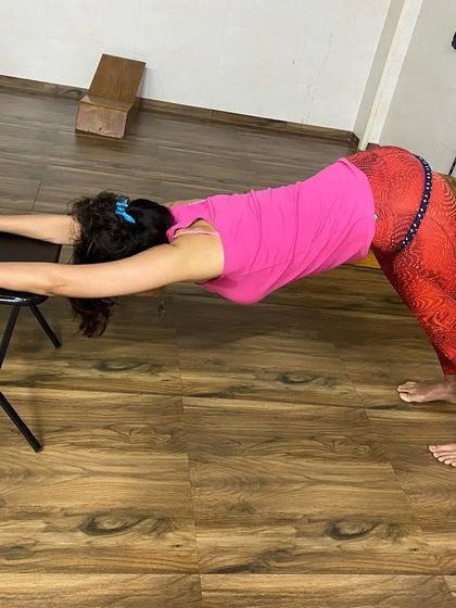 Using a chair and wall rope to add traction in a supported Downward-Facing Dog. The rope around the hips gently pulls the body back, deepening the stretch.