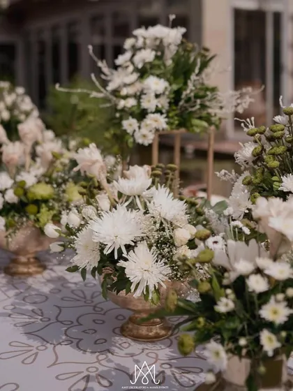 A collection of beautiful white chrysanthemums and other blooms in ornate gold vases, used as part of the table centerpieces.