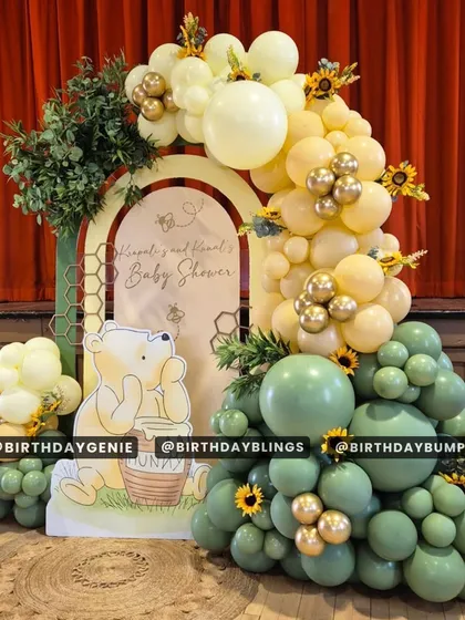 The full view of the Winnie the Pooh baby shower setup, with a beautiful balloon arch over a custom backdrop. The red curtain in the background adds a touch of elegance.