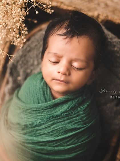 A precious newborn wrapped snugly in a green swaddle, resting in a basket. The simplicity of the setup allows the baby's peaceful expression to be the star.