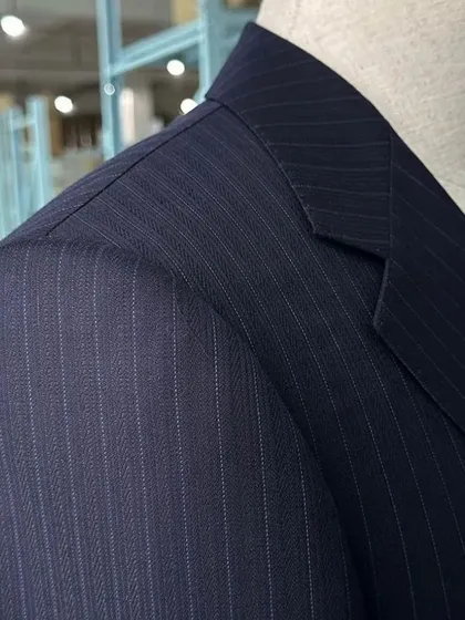 The shoulder construction is critical to a suit's silhouette. This close-up of a navy pinstripe blazer shows the clean lines and structured shoulder we achieve through meticulous tailoring.
