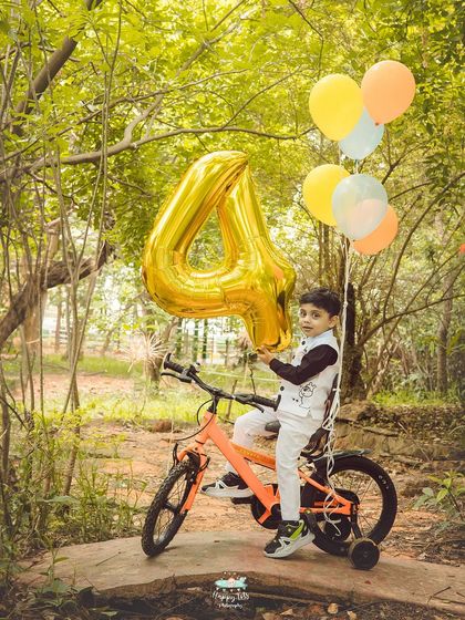 A full shot of the birthday boy posing proudly with his bike and balloon. The natural environment adds a sense of adventure to the portrait.