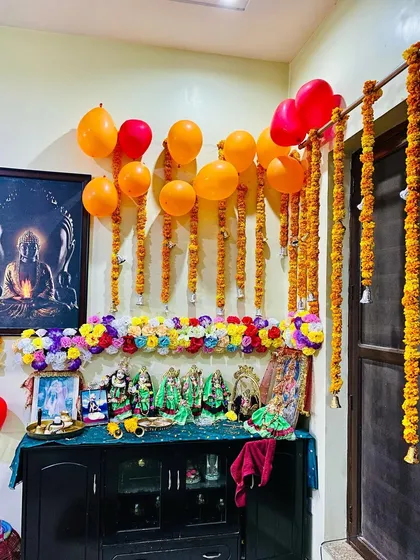 Another view of the decorated pooja space, highlighting the fresh marigold strings hanging next to the door and the arrangement of deities on the cabinet.