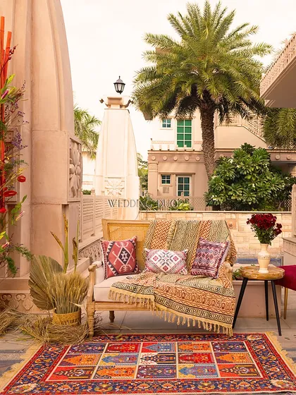 A Mehendi setup that speaks the language of joy. This cozy corner at ITC Grand Bharat combines a colorful patchwork rug, printed cushions, and a pop of red from bamboo sticks and florals.