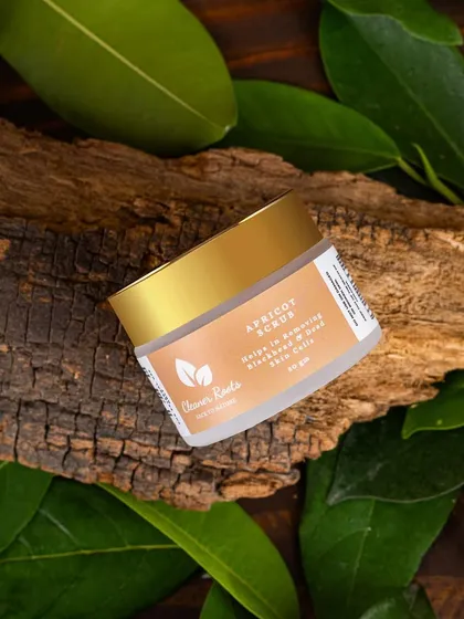 An earthy, natural shot of Cleaner Roots' Apricot Scrub, placed on a piece of bark and surrounded by green leaves. This styling is perfect for organic and natural skincare brands.