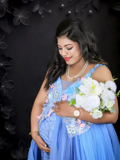 A beautiful close-up portrait of the mom-to-be. She holds a white bouquet, and the dark background with subtle floral details highlights her radiant expression.