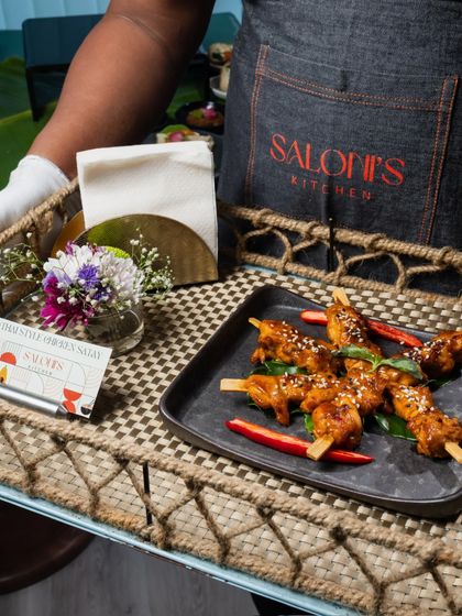 It's all in the details. A server presents Thai Style Chicken Satay on a rustic woven tray, complete with a business card and a small floral arrangement.
