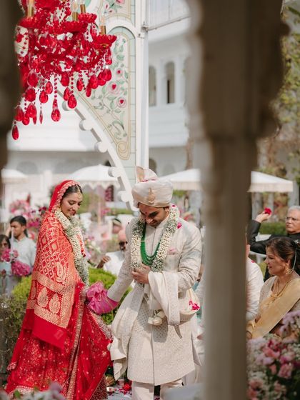 A beautiful moment from the wedding ceremony, framed by the venue's architecture. The red of the bride's lehenga and the chandelier pop against the soft pastels of the floral decor.