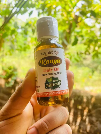 A bottle of Kanya Hair Oil held against a natural, leafy background, highlighting its connection to nature.