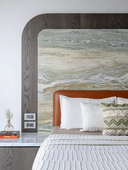 A close-up of the layered textures in the bedroom, with a rough stone slab, a dark wood frame, and a soft leather headboard.