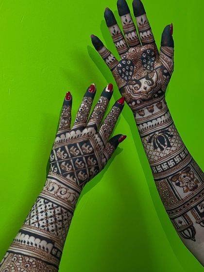 A full-arm bridal design with a variety of symbols, including a portrait, swastikas, and elephants, against a vibrant green background.