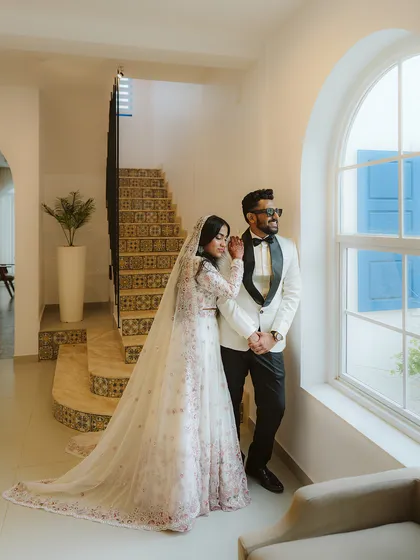 A moment of quiet elegance. Aysha and Ramzil look out from a window in a beautiful, light-filled space, creating a classic and sophisticated wedding portrait.