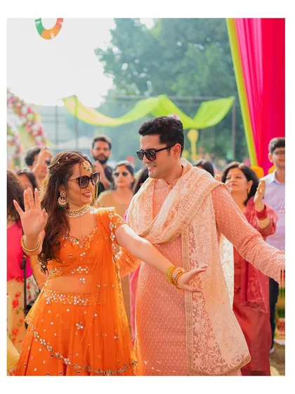 The couple dances joyfully with their guests, capturing the high energy and fun of a Mehendi party.