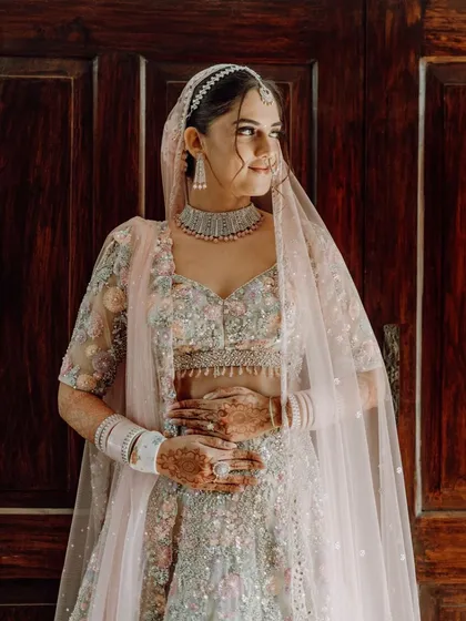 A beautiful three-quarter portrait of the bride in her pastel lehenga, standing against a wooden door.