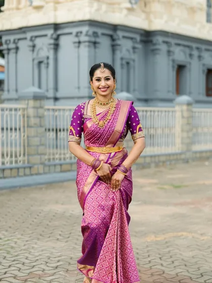A full-length shot of a bride in a purple Kanchipuram saree, standing in front of a temple. This image captures the timeless elegance of a traditional South Indian bridal look.