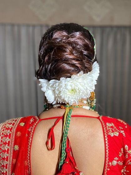 A classic bridal updo with a large bunch of white chrysanthemums. This is a bold and beautiful choice that pairs wonderfully with a traditional red lehenga.