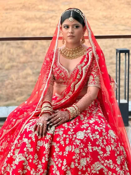 A seated portrait of the bride in her red lehenga, looking serene and beautiful. Her soft glam makeup with a defined eye and neutral lip enhances her features without overpowering her.