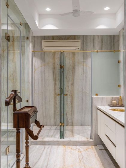 A spacious walk-in shower with glass doors and brass fittings continues the bathroom's theme of opulent materiality. The book-matched marble on the far wall creates a dramatic, symmetrical pattern.