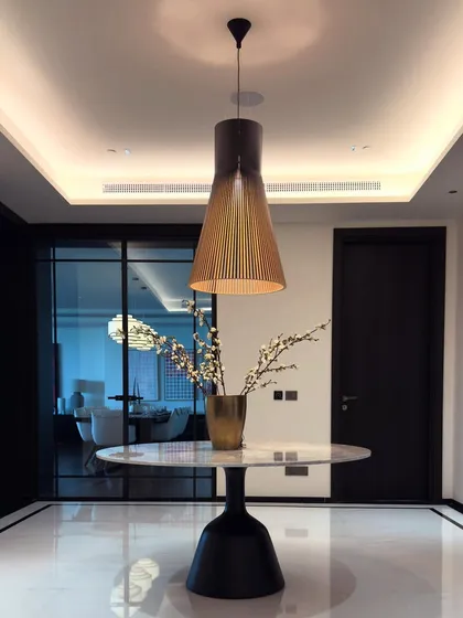 This foyer is a study in minimalism and understated luxury. We used white marble flooring with delicate black borders to create a clean, polished foundation. The sculptural pedestal table and the elegant wooden pendant light serve as a striking focal point, demonstrating how simple, high-quality elements can define a space.