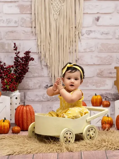 A happy harvest day at our pumpkin farm. This little girl in her bright yellow dress is all smiles while sitting in a rustic wagon, part of our detailed autumn-themed setup.